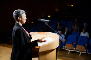 Female business executive giving a speech at conference center.